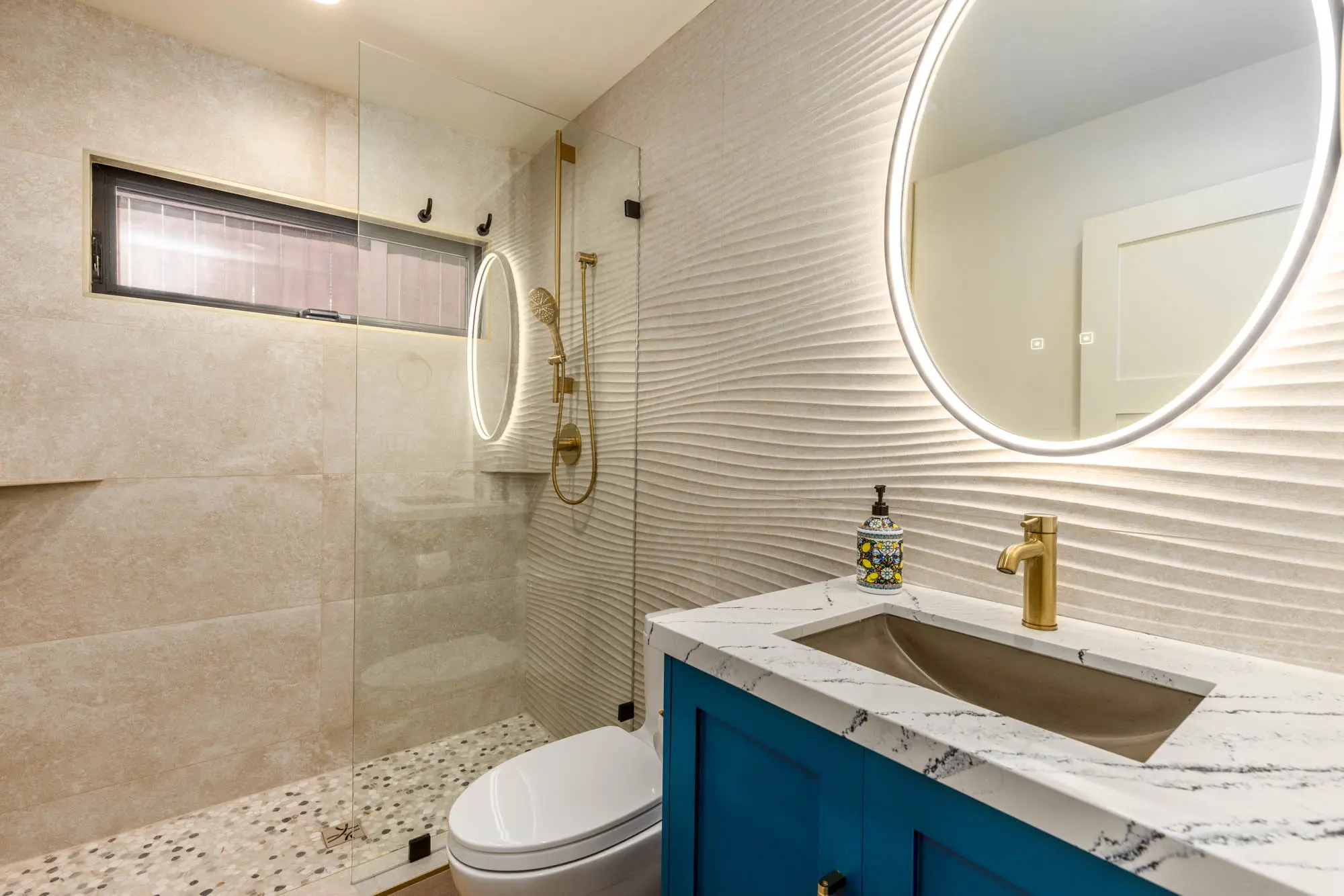Bathroom remodeling with a 3D wave wall, blue vanity, and gold hardware by Teknik