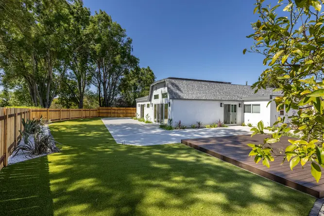 Modern white home with a gambrel roof, concrete patio and lush sun-drenched lawn